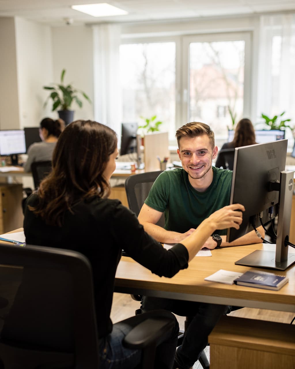Zwei Personen lächeln gemeinsam vor einem Bildschirm im Büro